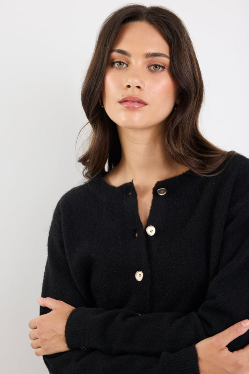 Woman wearing a black cardigan with gold buttons against a white background
