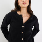 Woman wearing a black cardigan with gold buttons against a white background