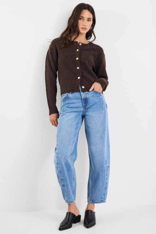 Woman wearing a brown button-up shirt and blue jeans on a white background