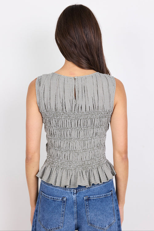 Woman wearing a sleeveless khaki checkered top with shirring through the bodice and blue jeans.