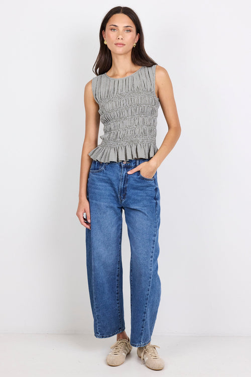 Woman wearing a sleeveless khaki checkered top with shirring through the bodice and blue jeans.