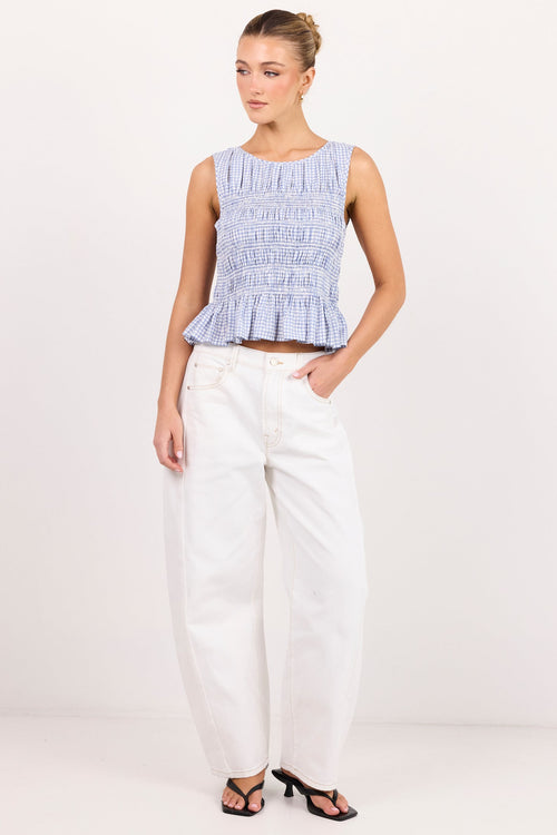 A woman modeling a sleeveless light blue and white smocked crop top paired with white wide-leg pants and black sandals, standing against a plain white studio background.