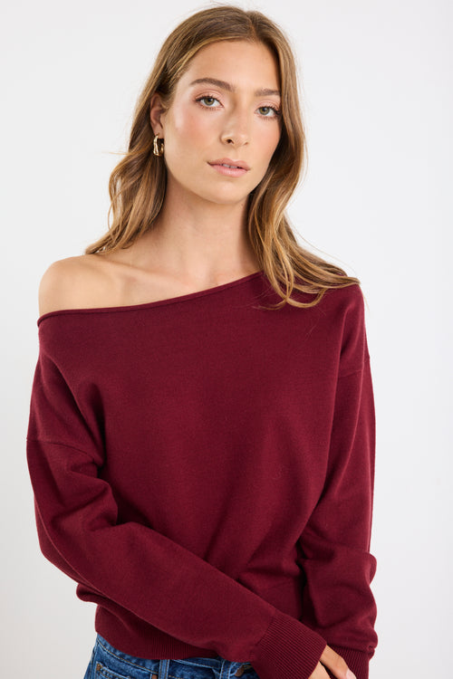 Woman wearing a burgundy off-shoulder sweater against a white background