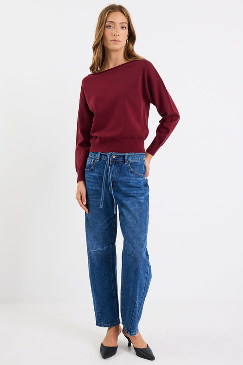 Woman wearing a burgundy sweater and blue jeans on a white background