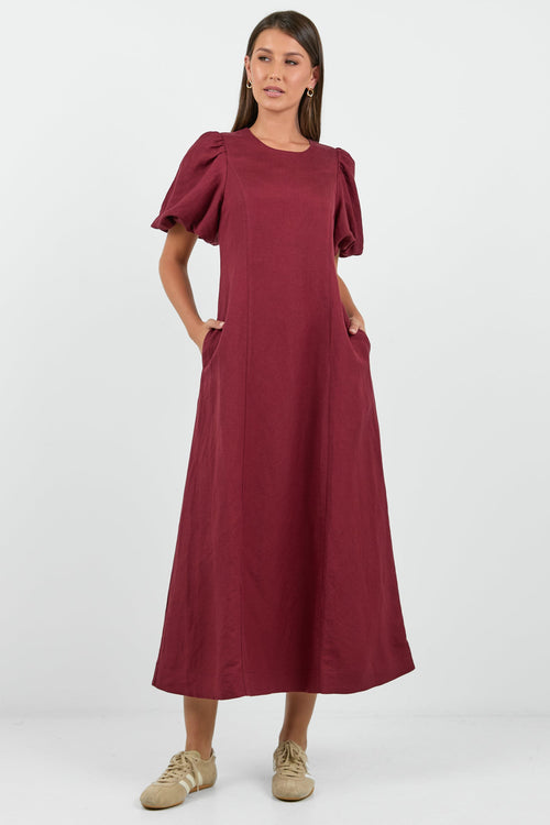 Woman wearing a burgundy dress with puff sleeves on a white background