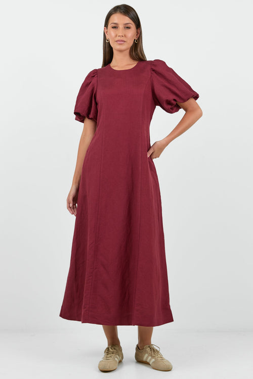 Woman wearing a burgundy dress with puff sleeves on a white background