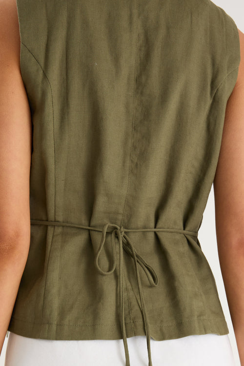 the model wears a green linen vest with a white maxi skirt