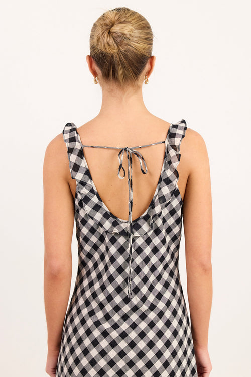 A woman viewed from the back wearing a sleeveless black and white gingham dress with a tie-back neckline, set against a plain white studio background.