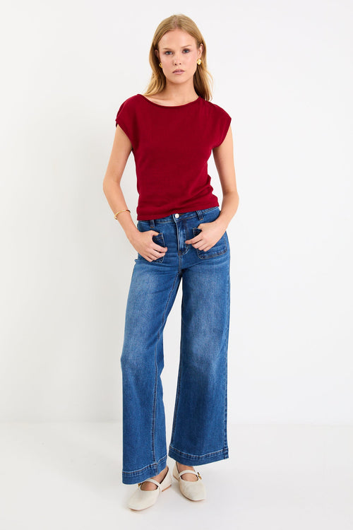 Model wearing a cherry red sleeveless knit top with a boatneck neckline