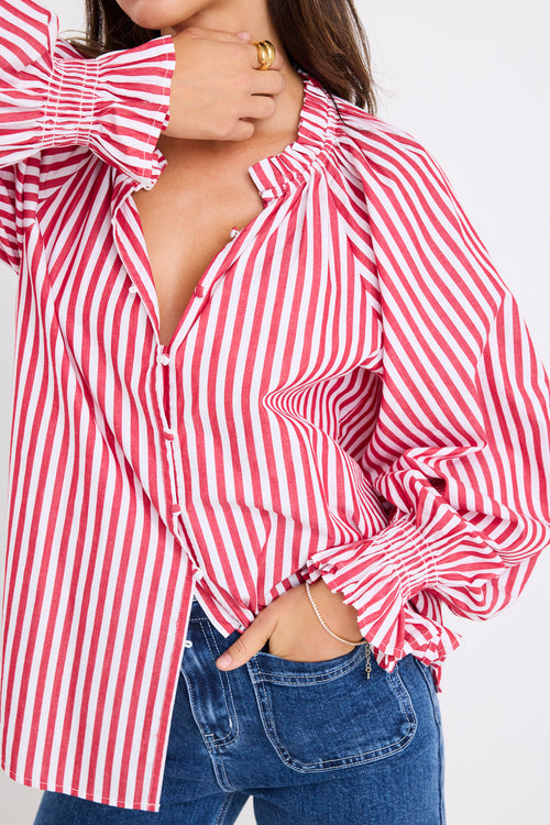 Model wears a red and white striped long sleeve shirt with button down front. 