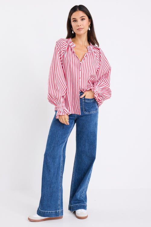 Model wears a red and white striped long sleeve shirt with button down front. 