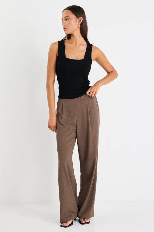 Woman wearing a black tank top and brown high-waisted pants on a white background