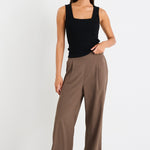 Woman wearing a black sleeveless top and brown high-waisted pants on a white background