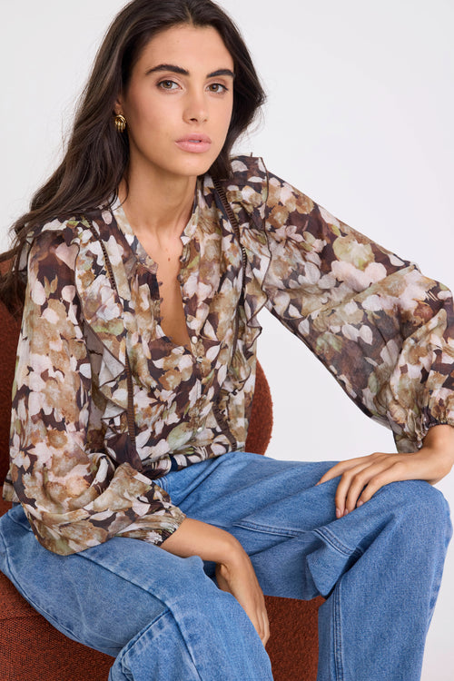 Woman wearing a floral blouse and blue jeans sitting on a chair.