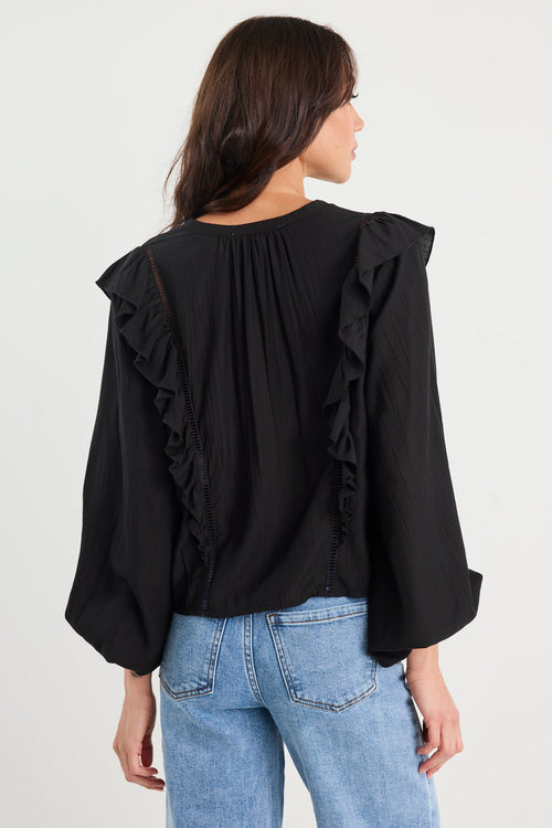 Person wearing a black blouse with ruffled sleeves and light blue jeans on a white background