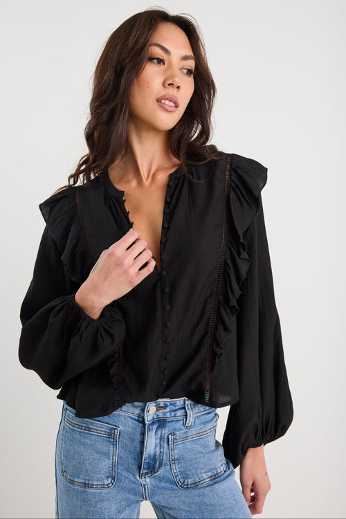 Woman wearing a black blouse with ruffled sleeves and blue jeans on a white background