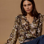 Woman wearing a floral blouse and blue jeans against a beige background