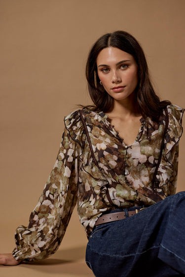 Woman wearing a floral blouse and blue jeans against a beige background