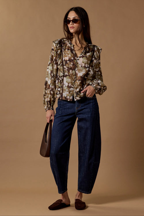 Woman wearing a patterned blouse and blue pants against a brown background