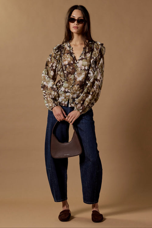 Woman wearing a floral blouse and sunglasses, holding a handbag against a beige background