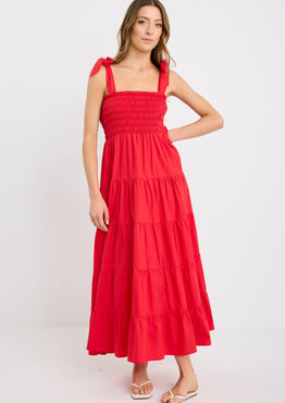 Woman wearing a cherry red tiered maxi dress with shirred bodice and strappy tie shoulders, styled with flat sandals.