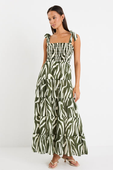 Model wearing a bold khaki zebra print dress with strappy tie details, a shirred bodice, and a tiered design. 