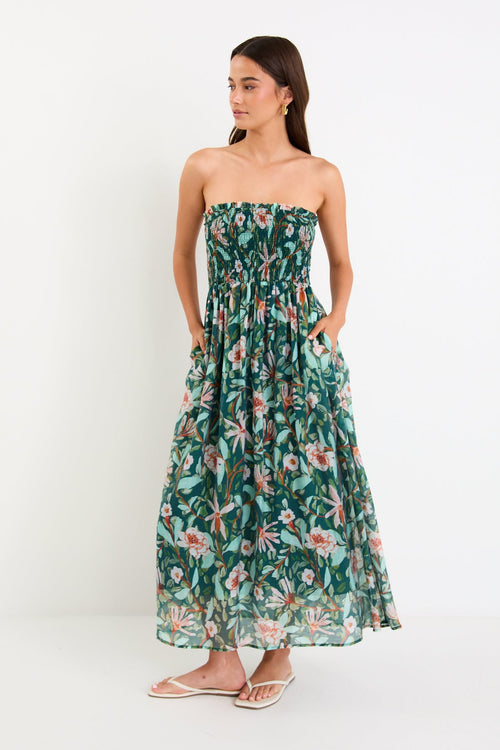 Model wearing a green forest-floral shirred midi dress with thin removable straps and a flowy skirt