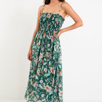 Model wearing a green forest-floral shirred midi dress with thin removable straps and a flowy skirt