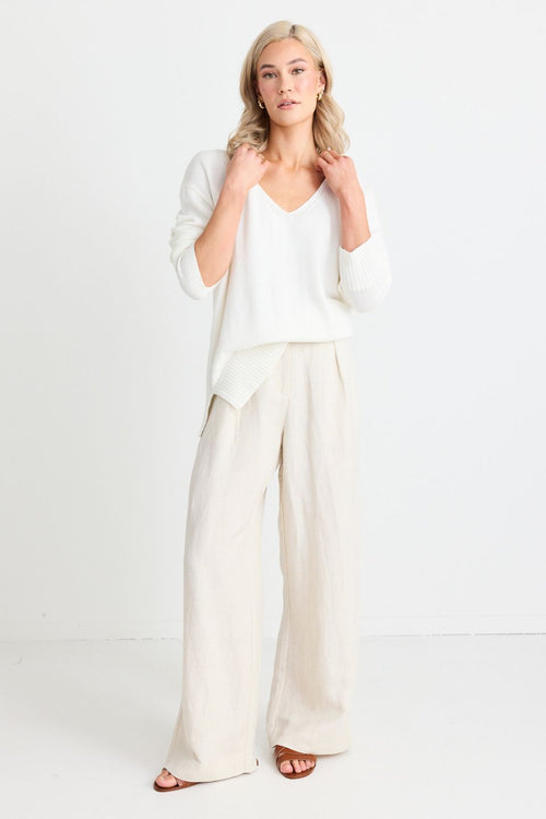 model wears natural linen pants and a white jumper and sandals