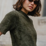 Woman wearing a green sweater and sunglasses with a blurred background