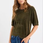 Woman wearing an olive green sweater and blue jeans on a white background