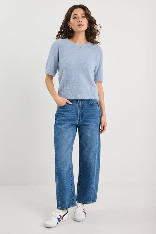 Woman wearing a light blue sweater and jeans on a white background