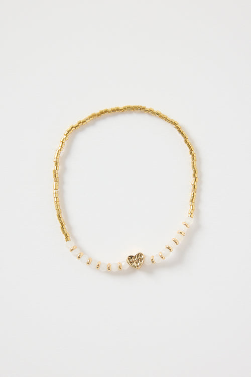 Ivory and gold beaded bracelet with a small heart charm, featuring gold cube beads and ivory accents. Delicate women’s jewellery perfect for gifting or stacking, photographed on a clean white background
