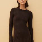 Woman wearing a black ribbed dress against a beige background
