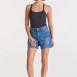 Woman wearing a black tank top and blue denim shorts on a white background