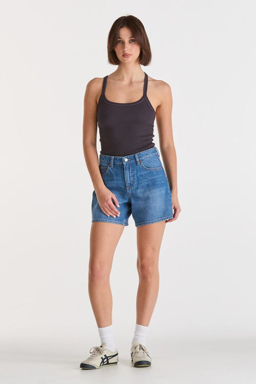 Woman wearing a black tank top and blue denim shorts on a white background