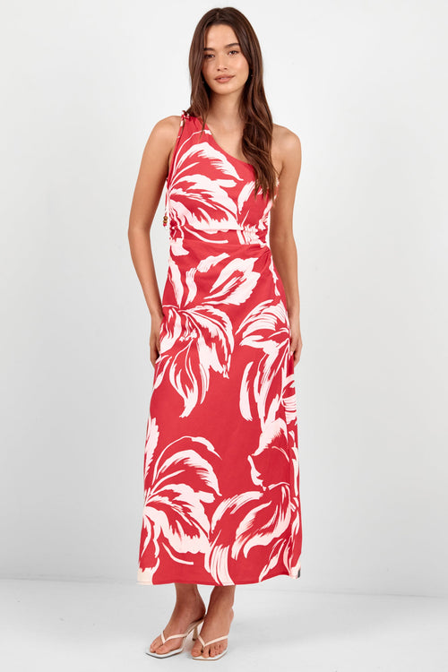 A woman modeling a sleeveless red maxi dress with a bold white tropical leaf pattern, standing against a plain light gray studio background.