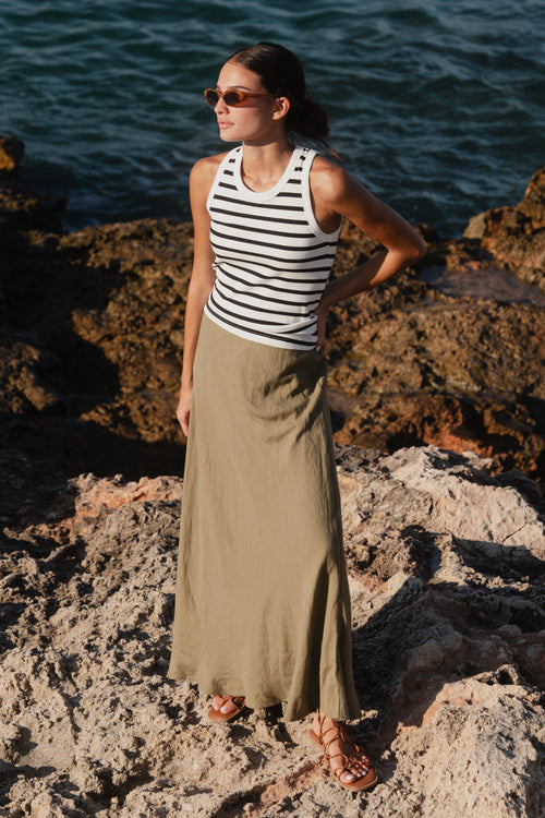 model wears a striped tank and a green linen maxi skirt by the beach