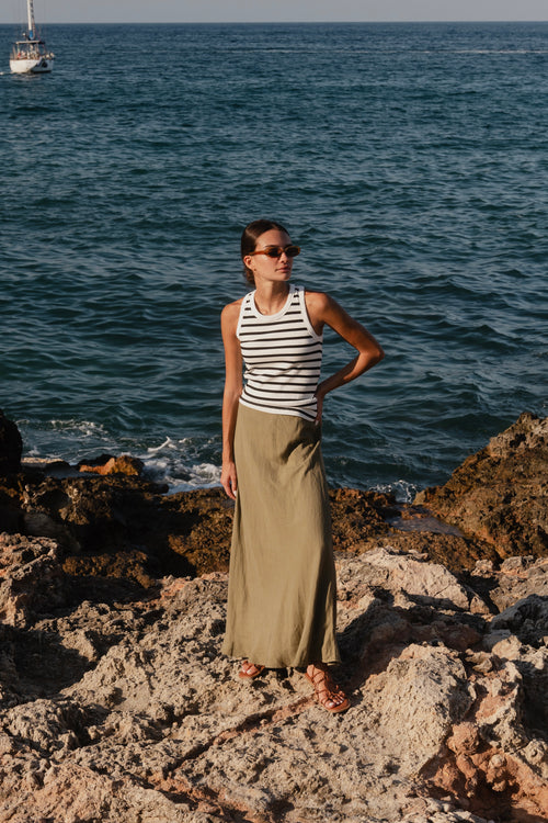 model wears a striped tank and a green linen maxi skirt by the beach