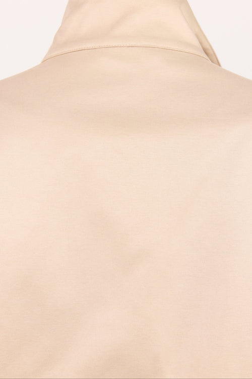 Close-up of a beige or cream-colored garment, showing the back of a high-neck top or turtleneck with a smooth matte finish.