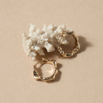 Gold hoop earrings on a beige surface with white coral-like object