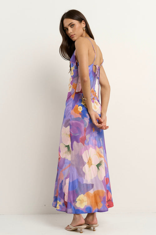 Woman wearing a bias-cut violet floral slip dress with spaghetti straps and abstract flower print.