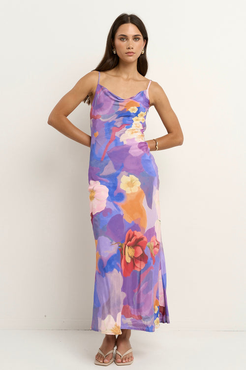 Woman wearing a bias-cut violet floral slip dress with spaghetti straps and abstract flower print.