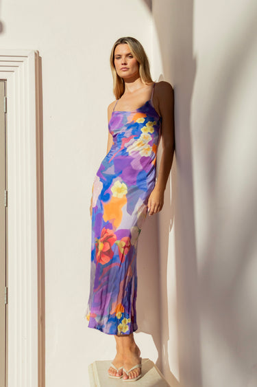 Woman wearing a bias-cut violet floral slip dress with spaghetti straps and abstract flower print.
