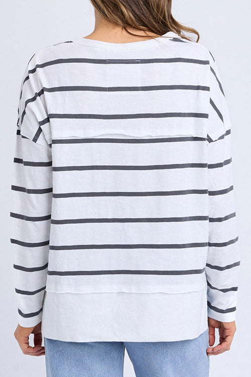 Woman wears a white long sleeve top with black horizontal stripes, crew neck, exposed stitching, and a relaxed fit. Styled with blue jeans for a casual, easy-going look.