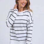Woman wears a white long sleeve top with black horizontal stripes, crew neck, exposed stitching, and a relaxed fit. Styled with blue jeans for a casual, easy-going look.