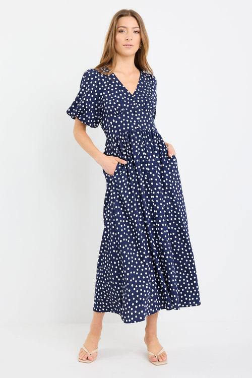 Woman wearing a navy blue dress with white polka dots on a white background