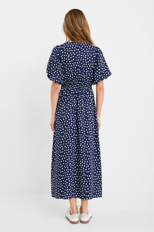 Woman wearing a navy dress with white polka dots on a white background