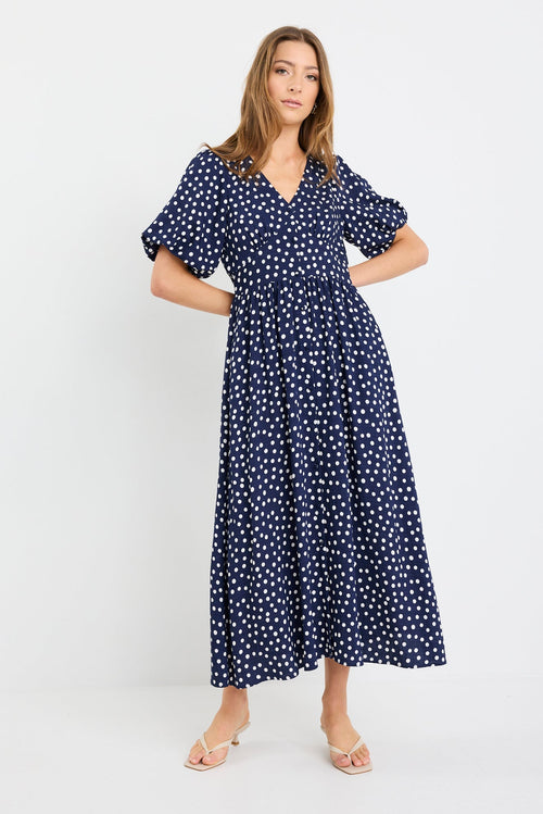 Woman wearing a navy blue dress with white polka dots on a white background