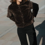 Woman wearing a brown fur coat standing on a stone pavement.